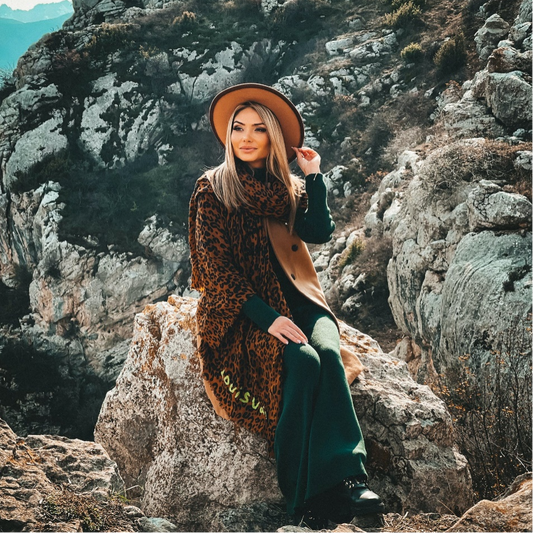 A woman sitting on the rock wearing a leopard scarf
