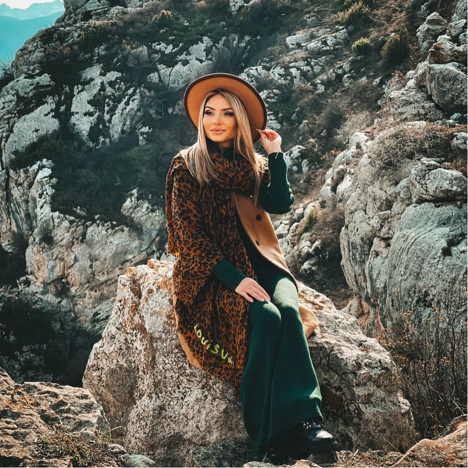 A woman sitting on the rock wearing a leopard scarf 