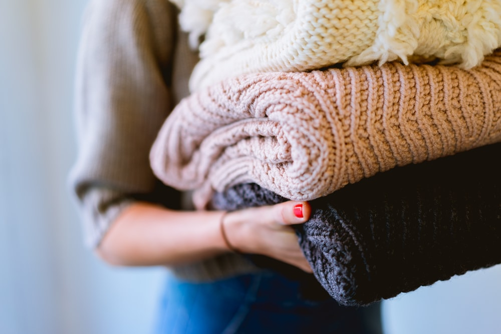 A woman holding different colored sweaters 