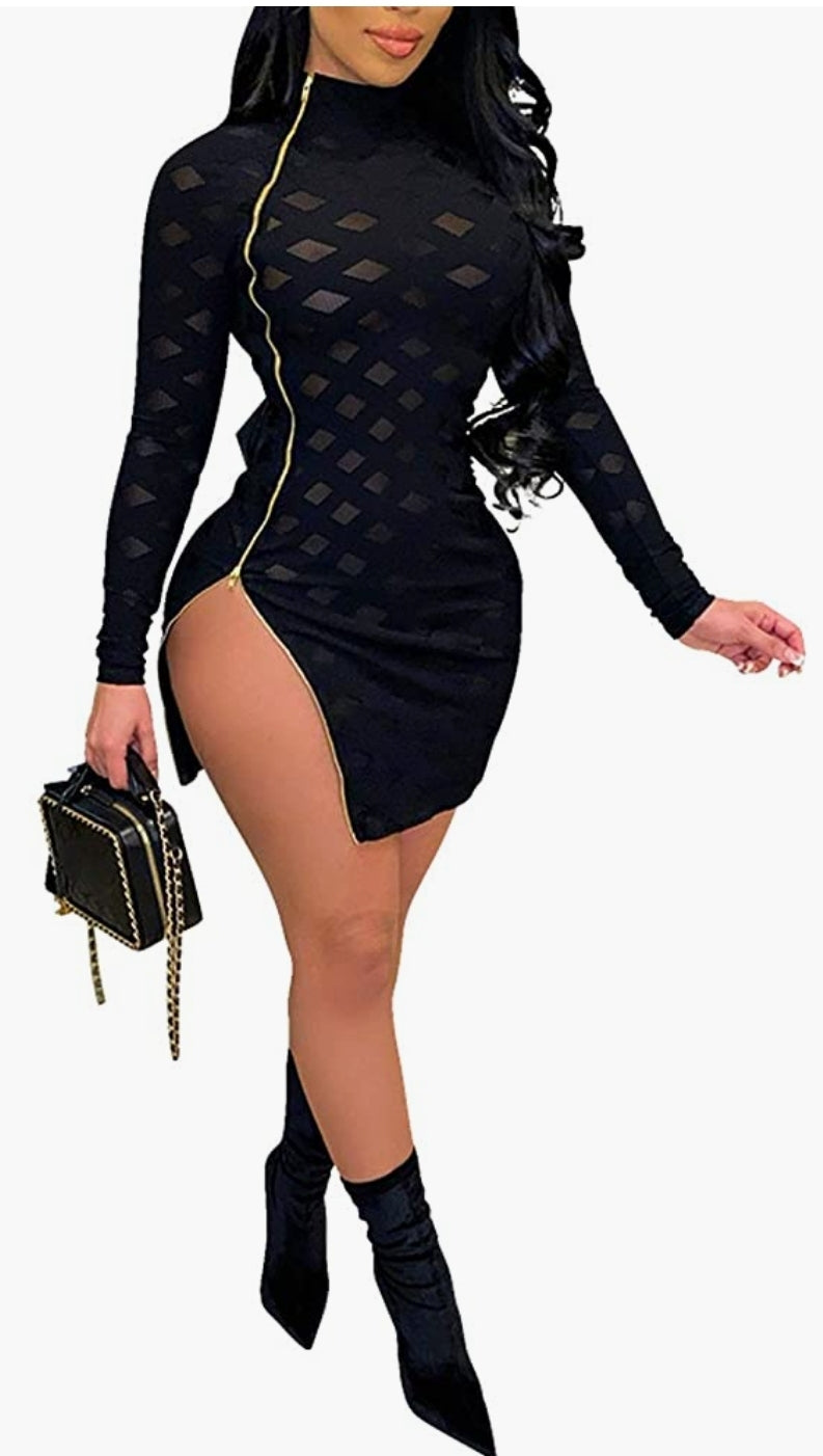 Lady standing in long sleeve sheer black ,mesh and spandex dress holding black and gold chain purse. Dress has zipper that runs from the neckline to bottom to adjust as you wish.  She paired the dress with black booties to finish the look.
