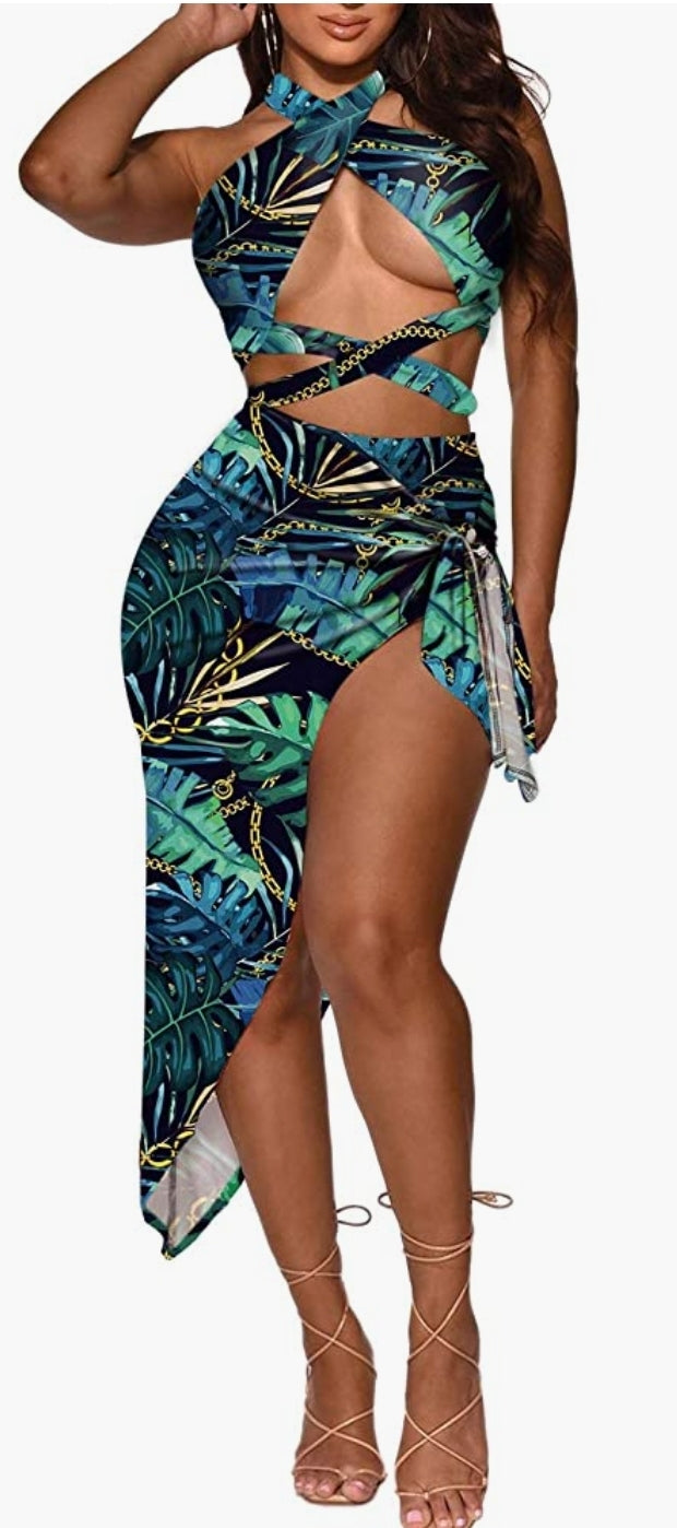 Women in blue and green palm leaf two piece swimsuit that has chains in the pattern with the leaves.  She has a cover up around her legs and tied at the waist. The top crisscross around her neck and underneath her breast.  The bottoms of the swim suit is high waist to meet the top.  She pair the swim suit and cover up with beige strap sandals that tie up just below her calves.