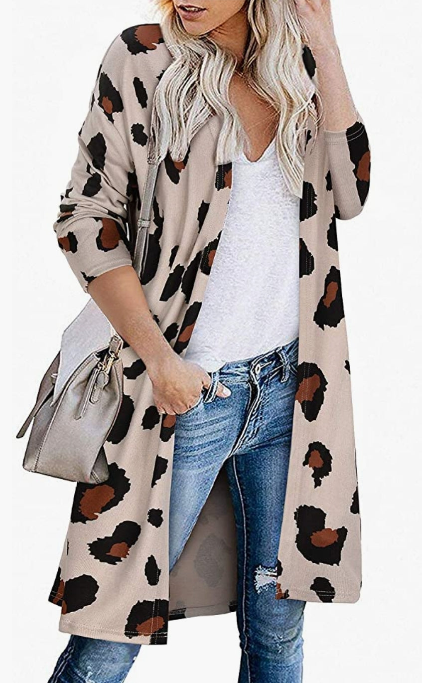 Woman standing in light cream leopard print cardigan, white t-shirt and jeans. One hand in her front pocket with her thumb in front belt loop and the other hand fondling her hair . She paired the look with over sized beige purse .